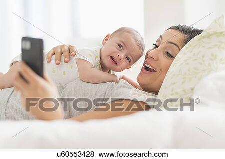 Stock Photo - Mother photographing herself and baby boy (2-5 months) with cell phone. Fotosearch