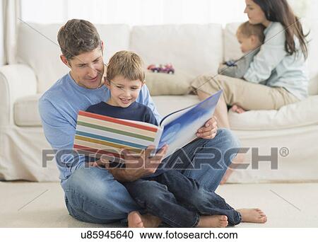 Stock Image - Parents with kids (12-17 months, 6-7) at home, father reading to son. Fotosearch