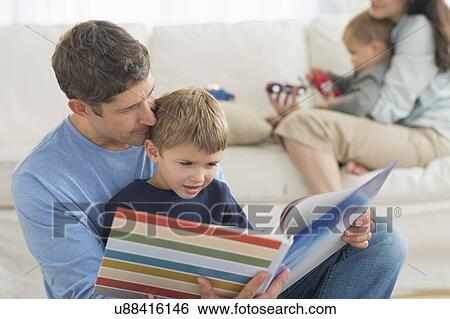 Stock Photograph - Parents with kids (12-17 months, 6-7) at home, father reading to son. Fotosearch