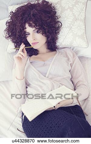Stock Image - Portrait of beautiful brunette woman lying on bed with diary. Fotosearch