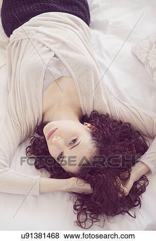Stock Photo - Portrait of beautiful brunette woman lying on bed. Fotosearch