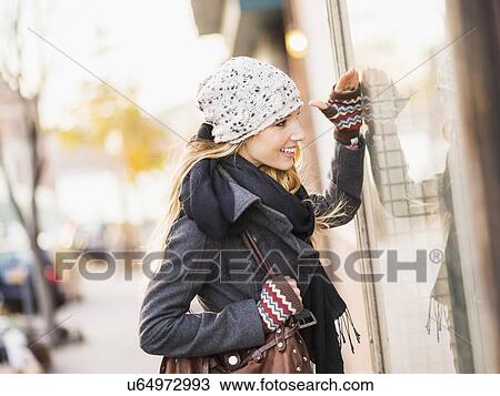 Stock Image - Portrait of blond woman looking at window display. Fotosearch