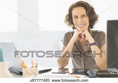 Stock Image - Portrait of business woman sitting at desk. Fotosearch