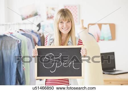 Stock Image - Portrait of female business owner holding open sign. Fotosearch