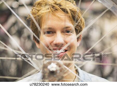 Stock Image - Portrait of man behind bike wheel. Fotosearch