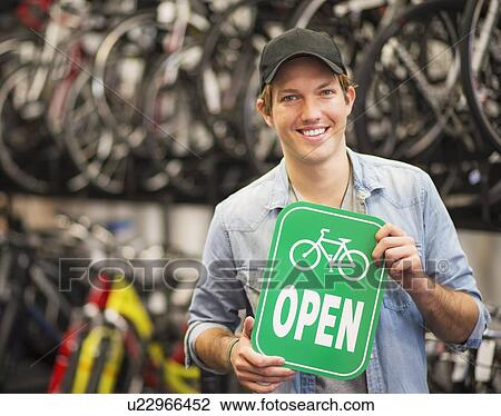 Portrait of man in bike shop holding open sign View Large Photo Image Stock Image - Portrait of man in bike shop holding open sign. Fotosearch