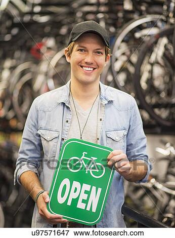 Portrait of man in bike shop holding open sign View Large Photo Image Stock Photo - Portrait of man in bike shop holding open sign. Fotosearch