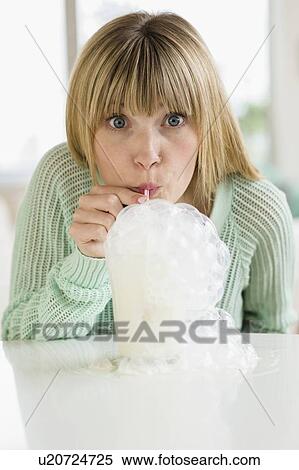 Stock Photography - Portrait of woman blowing bubbles in milkshake. Fotosearch