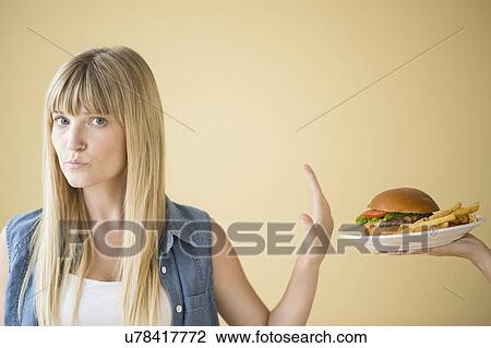 Stock Image - Portrait of woman rejecting hamburger that is being offered to her. Fotosearch