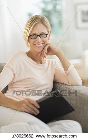 Portrait of woman sitting on sofa holding tablet pc View Large Photo Image Stock Image - Portrait of woman sitting on sofa holding tablet pc. Fotosearch