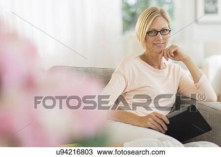 Portrait of woman sitting on sofa holding tablet pc View Large Photo Image Stock Image - Portrait of woman sitting on sofa holding tablet pc. Fotosearch