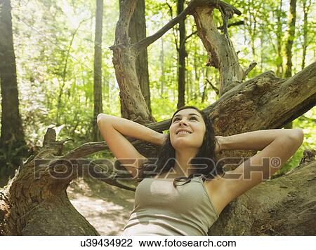 Stock Image - Portrait of young woman lying down on log. Fotosearch