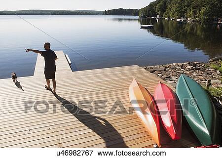 Stock Photo - Rear view of man standing on jetty pointing at something. Fotosearch
