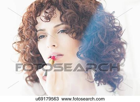 Stock Image - Studio shot of beautiful woman applying lipstick. Fotosearch
