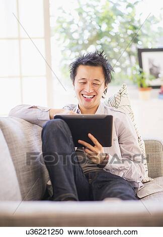 Stock Image - Teenage boy (16-17) sitting on sofa and using digital tablet. Fotosearch