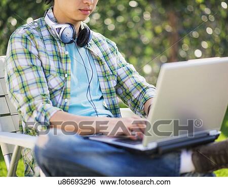 Stock Photograph - Teenage boy (16-17) using laptop in park, mid-section. Fotosearch