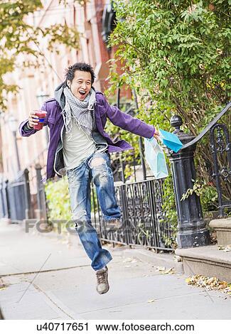 Stock Image - Teenage boy (16-17) with shopping bags drinking smoothie. Fotosearch