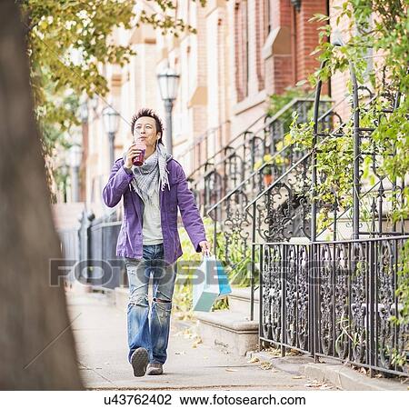 Stock Image - Teenage boy (16-17) with shopping bags drinking smoothie. Fotosearch