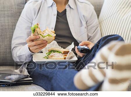 Teenage boy(16-17) eating sandwich and watching tv View Large Photo Image Picture - Teenage boy(16-17) eating sandwich and watching tv. Fotosearch