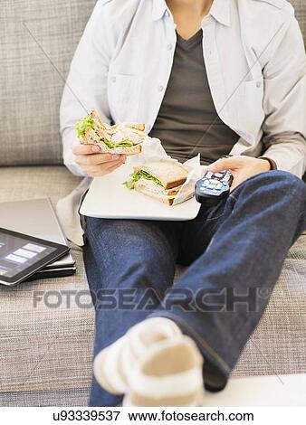 Stock Photo - Teenage boy(16-17) eating sandwich and watching tv. Fotosearch