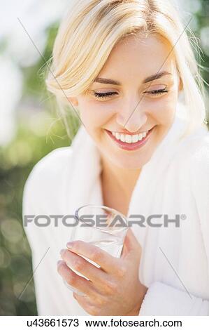 Stock Image - Teenage girl (16-17) wearing bathrobe drinking water. Fotosearch