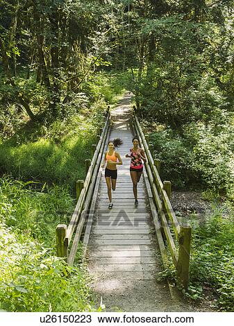 Stock Image - Two young women running over wooden footbridge. Fotosearch