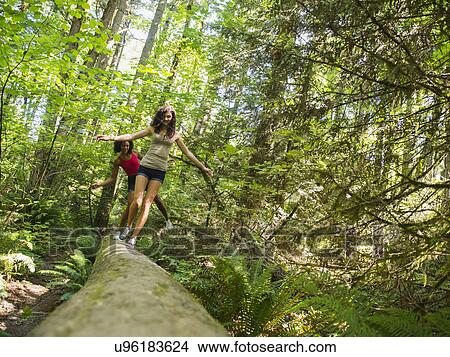 Picture - Two young women walking on log in forest. Fotosearch