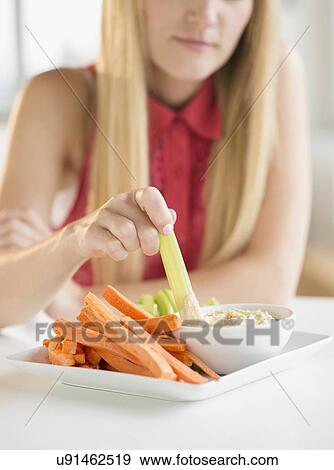 Stock Photo - Woman dipping celery. Fotosearch