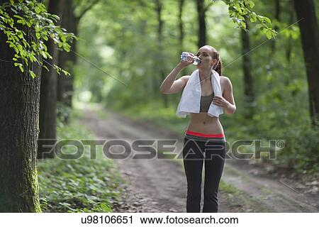 Woman drinking water during jogging in forest View Large Photo Image Stock Image - Woman drinking water during jogging in forest. Fotosearch