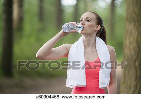 Woman drinking water during jogging in forest View Large Photo Image Stock Photo - Woman drinking water during jogging in forest. Fotosearch