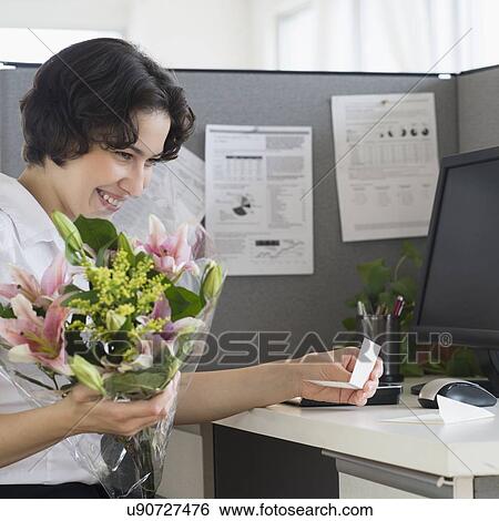 Stock Photograph - Woman holding bouquet in office. Fotosearch