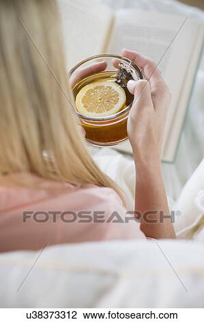 Stock Image - Woman holding tea cup and reading book. Fotosearch