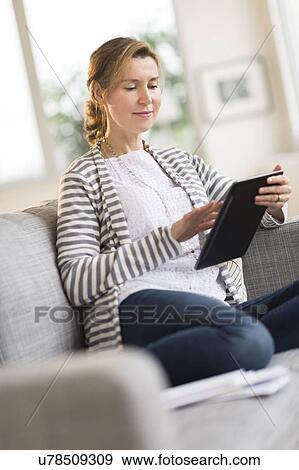 Woman sitting on sofa using tablet pc View Large Photo Image Stock Photo - Woman sitting on sofa using tablet pc. Fotosearch
