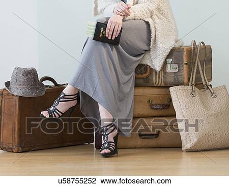 Stock Image - Woman sitting on stack of vintage suitcases. Fotosearch