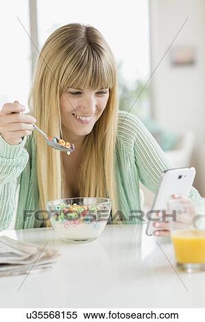 Woman using phone while eating cereal View Large Photo Image Stock Photography - Woman using phone while eating cereal. Fotosearch