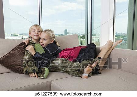 Stock Photo - Affectionate siblings in dinosaur and vampire costumes at home. Fotosearch
