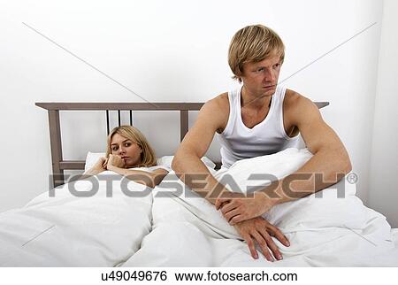 Stock Photograph - Angry man sitting on bed with woman in house. Fotosearch