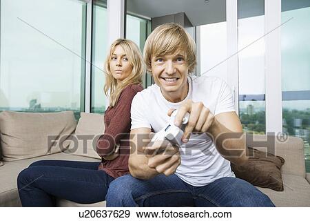 Stock Photo - Angry woman looking at man play video game in living room at home. Fotosearch