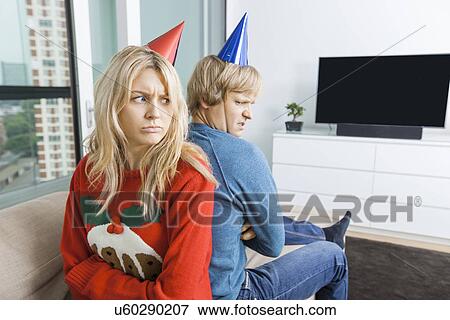 Annoyed couple in Christmas sweaters and party hats sitting back to back at home View Large Photo Image Stock Photo - Annoyed couple in Christmas sweaters and party hats sitting back to back at home. Fotosearch