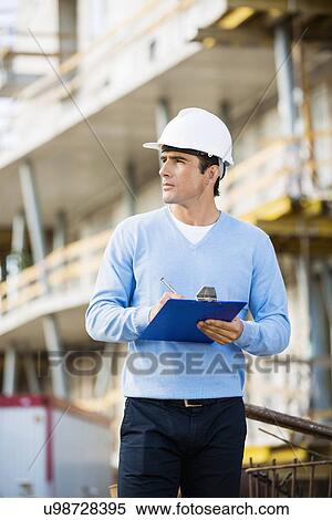 Stock Photography - Architect with clipboard and pen working at construction site. Fotosearch