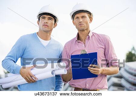 Stock Photo - Architects with blueprint and clipboard standing at site. Fotosearch