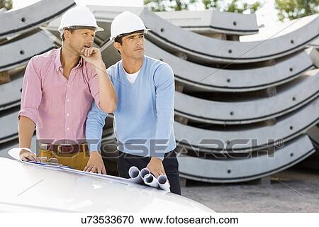 Stock Image - Architects with blueprints on car working at construction site. Fotosearch