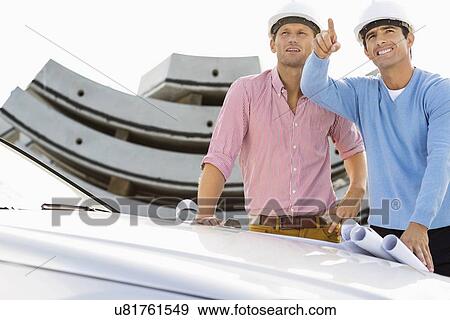 Architects with blueprints on car discussing at construction site View Large Photo Image Stock Photo - Architects with blueprints on car discussing at construction site. Fotosearch