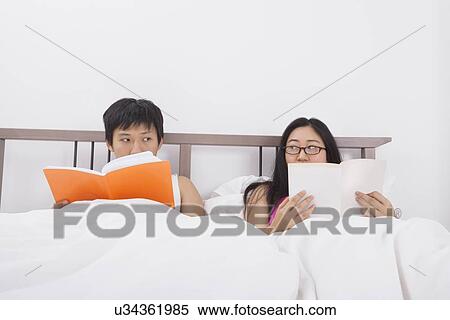 Stock Photography - Asian couple reading books while looking at each other in bed. Fotosearch