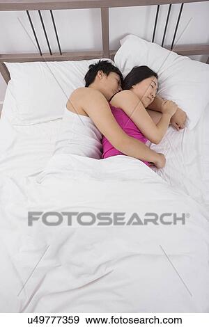 Stock Photo - Asian couple sleeping arm around in bed. Fotosearch