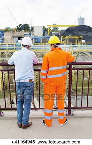 Stock Photography - Back view of architects standing against railing at construction site. Fotosearch