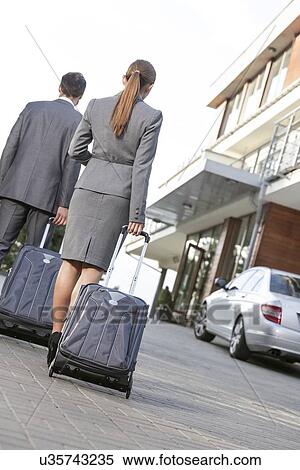 Stock Photography - Back view of business couple walking with luggage on driveway. Fotosearch