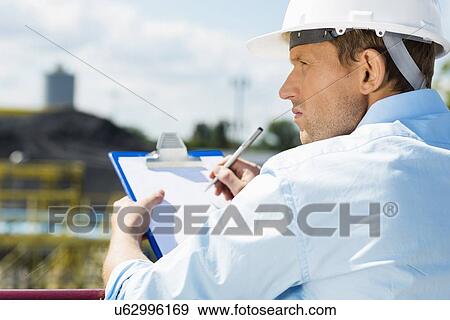 Stock Photo - Back view of male architect with clipboard at construction site. Fotosearch