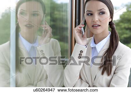 Beautiful businesswoman answering cell phone by glass door View Large Photo Image Stock Photo - Beautiful businesswoman answering cell phone by glass door. Fotosearch