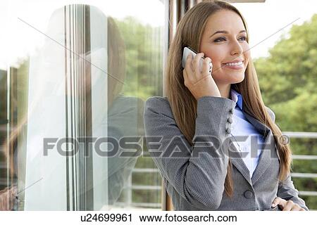 Stock Image - Beautiful businesswoman using cell phone by glass door. Fotosearch